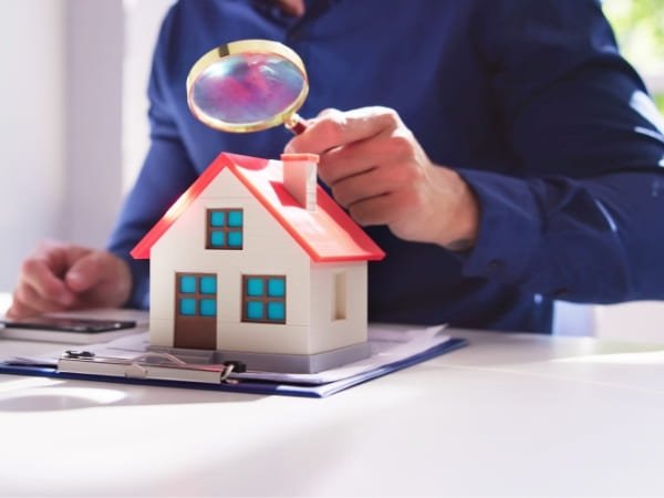 Une personne installée à un bureau examine une maquette de maison à l’aide d’une loupe, illustrant l’analyse de faisabilité d’un projet d’autonomie en eau et de récupération de l’eau de pluie.