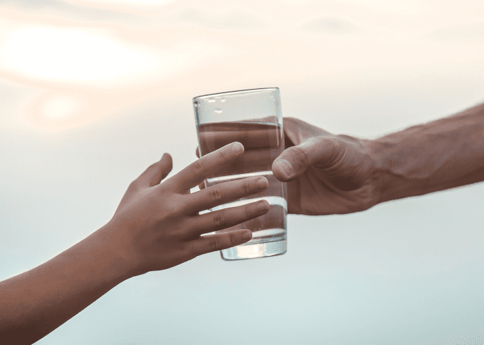 Transmission d’un verre d’eau entre un adulte et un enfant, illustrant l’accès à une eau de qualité et la préservation de la ressource pour les générations futures.