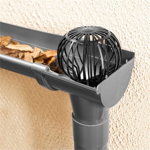 Crapaudine placée à la naissance d'une descente de gouttière — feuilles mortes accumulées autour, illustrant le risque de bouchon dans un système de récupération des eaux de pluie