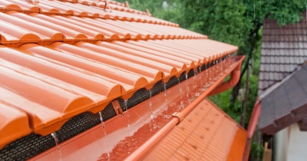 Récupération des eaux de pluie réglementation 2026 — toiture tuiles terre cuite et gouttière sous la pluie